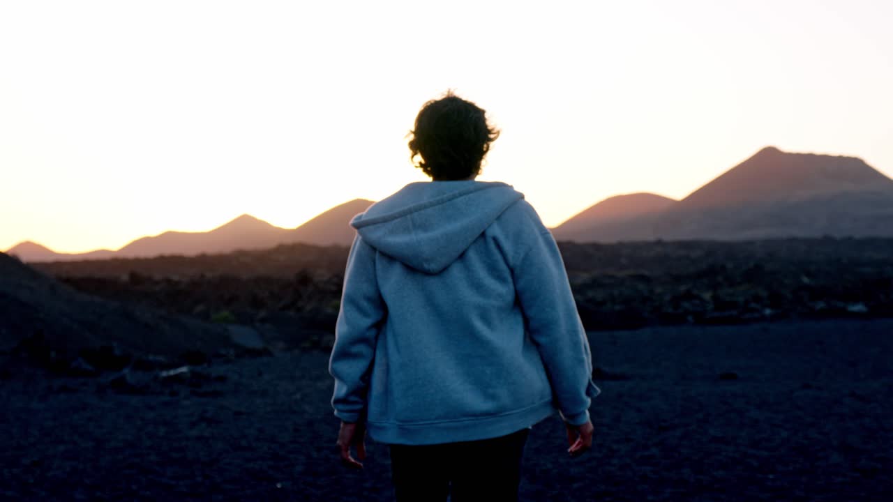 A lone man walks through the stark, volcanic landscape of the Volcán del Cuervo trail in Lanzarote, Canary Islands, Spain.
