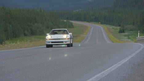camera pans out from behind guard rail to tracking a white sports car driving down a highway through the mountains.