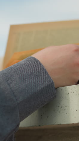 vista de mano de cerca de un individuo sosteniendo un libro en una valla mientras el viento sopla suavemente a través de las páginas, la mano descansa en el libro mientras el viento voltea las páginas