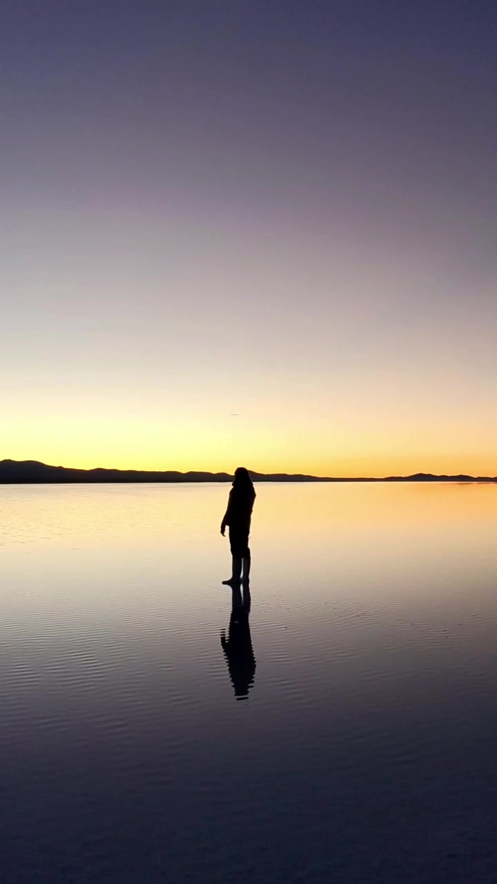 Bolivya'daki Uyuni Tuz Gölü'nde gün doğumu yansıması sırasında duran adam.