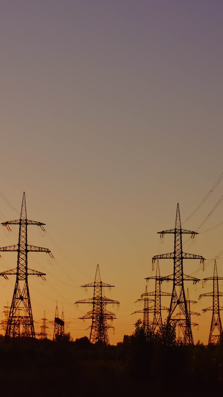Silhouette of high-voltage towers. Electricity pylons on energy station on the background of beautiful sky at sunset. Electricity station and high-voltage power lines.View from below. Vertical video