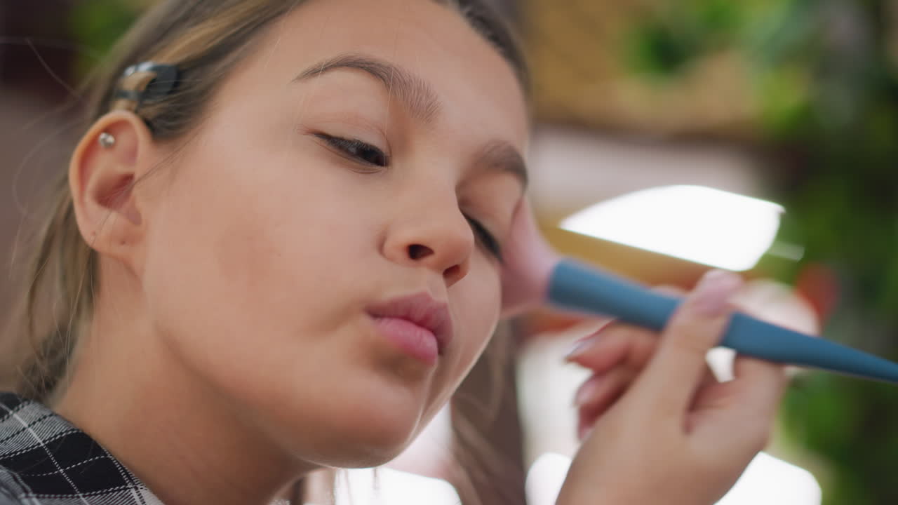 primer plano de una mujer joven ajustando su maquillaje usando un pincel, asegurando un retoque impecable en su cara, destacando su belleza y mejorando sus rasgos faciales para un aspecto pulido