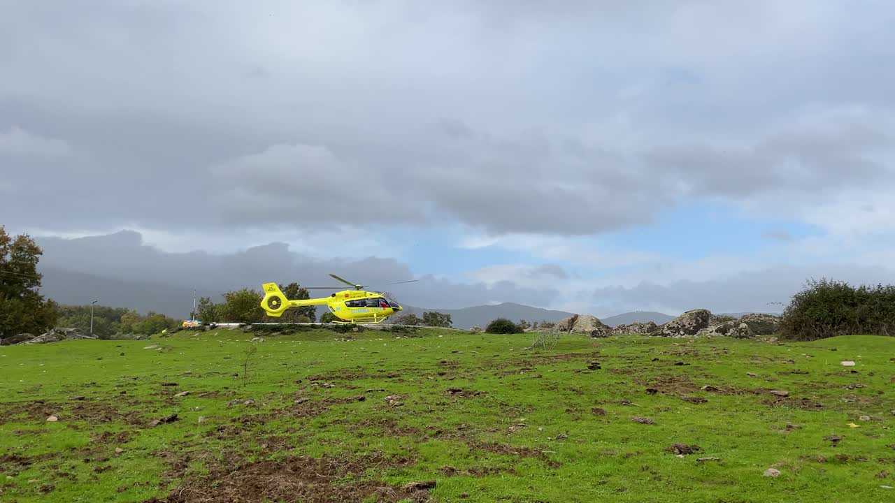 filming in a rural area of ​​the takeoff of a yellow emergency helicopter, we see the start on a platform and how it begins to rise, in the tree area there are some flashing lights of an ambulance