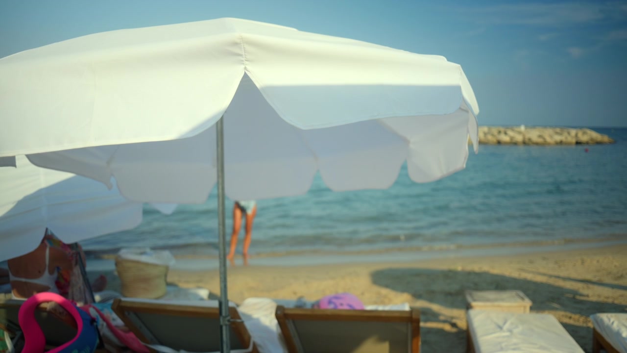 Ambiente da spiaggia rilassante con ombrelloni bianchi, lettini prendisole e onde marine calme, perfetto per vacanze estive e tempo libero.