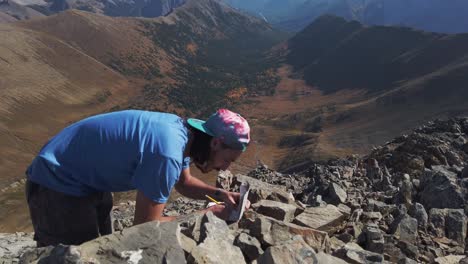 Hiker-writing-note-message-on-peak-of-the-mountain-over-valley-close-up-circled-Kananaskis-Alberta-Canada