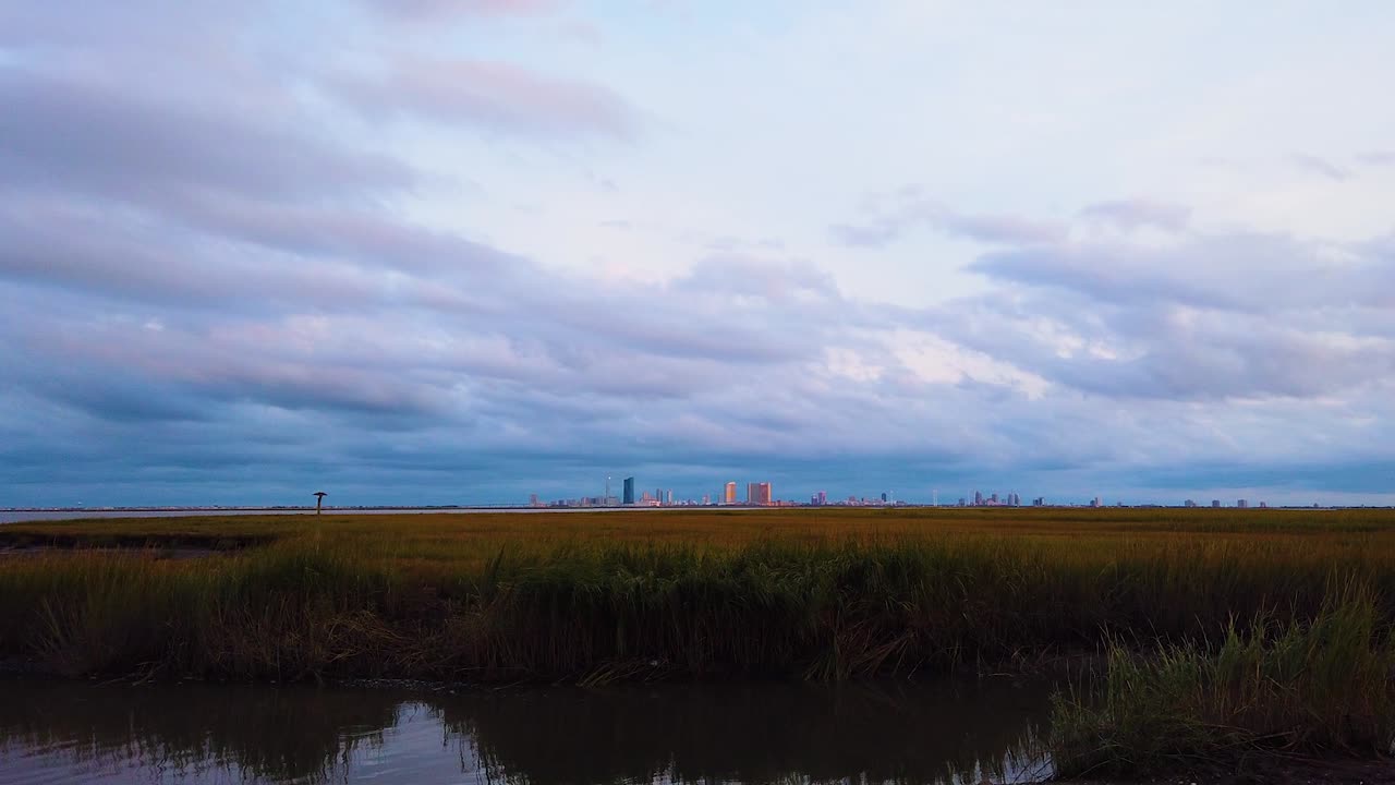 hd 모션랩스는 왼쪽에서 중앙으로 직선 이동하고 구름이 분홍색, 보라색, 파란색으로 변하면서 밤낮으로 대부분 흐린 하늘이 있는 수로를 통해 대서양 도시 스카이라인을 멀리 유지합니다.