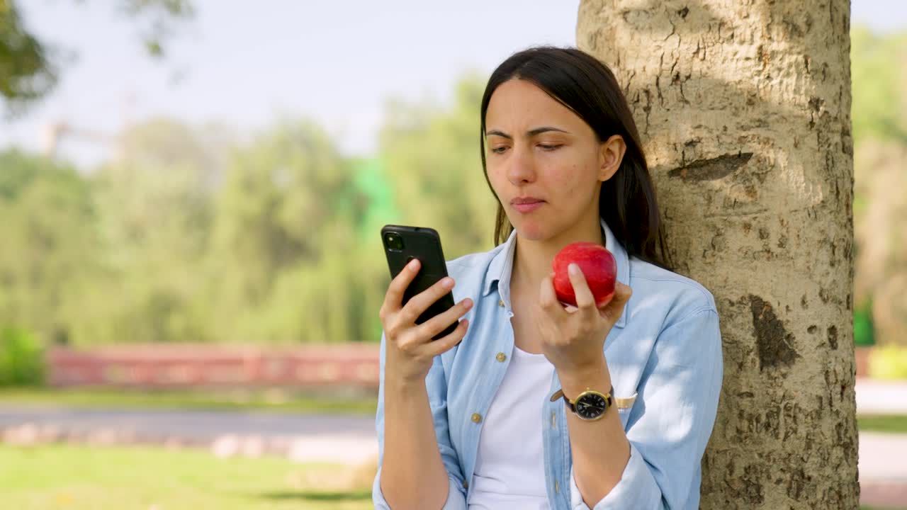 chica india comiendo manzana mientras usa el teléfono