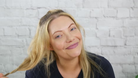 Happy-attractive-blonde-girl-playing-with-hair-cute-and-innocent-flirting-against-a-white-brick-wall