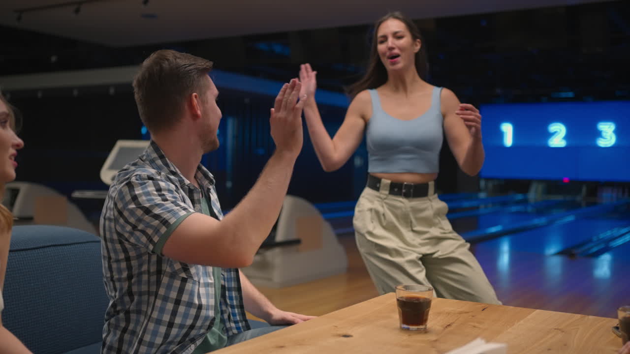 Una donna ispanica allegra in una sala da bowling corre felicemente dalle sue amiche per celebrare la serie di birilli abbattuti. Condividi la vittoria con gli amici. Gruppo di amici multietnico