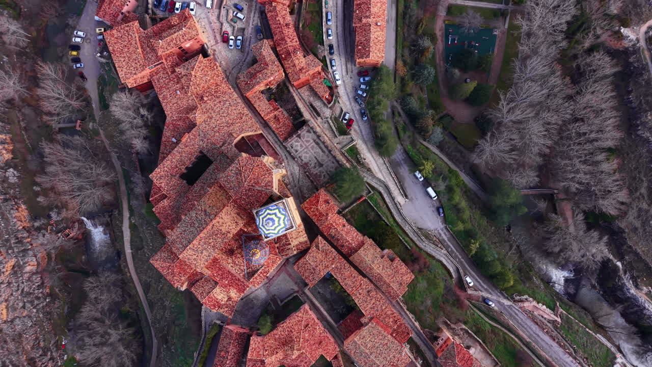 Top-down view of Albarracin's medieval rooftops with terracotta tiles, a decorated church dome, winding roads, and surrounding cliffs in Aragon, Spain