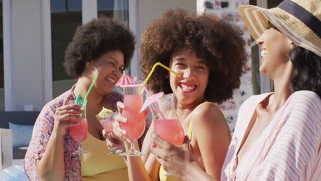 Happy-diverse-female-friends-making-toast-and-smiling-at-swimming-pool-party