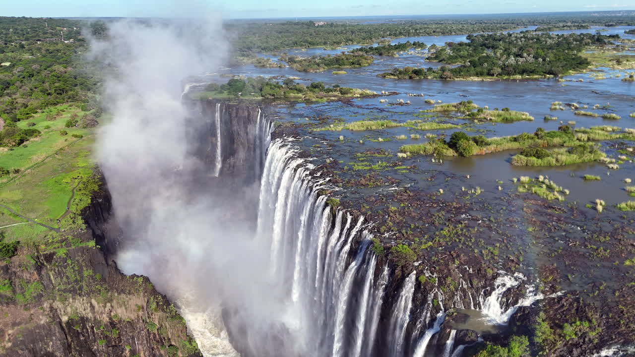 Aerial view of Victoria Falls with powerful waterfall plunging into gorge, mist rising above lush green forest, dramatic natural wonder and iconic travel destination in Africa