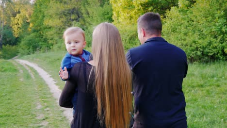 young family with a child is walking in the park, rear view. a young baby boy looks at the camera. healthy lifestyle