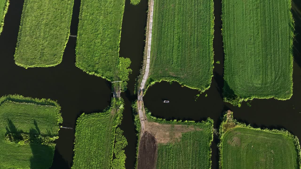 espectacular vista aérea de canales y vías fluviales en una tierra de pólder con aguas oscuras y campos verdes vivos, y un pequeño bote navegando en el agua, países bajos