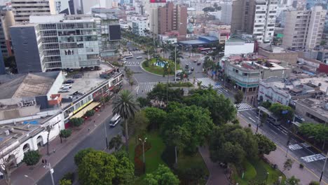 drone flies over public called "parque kennedy" filled with green trees. located in miraflores district of lima, peru.