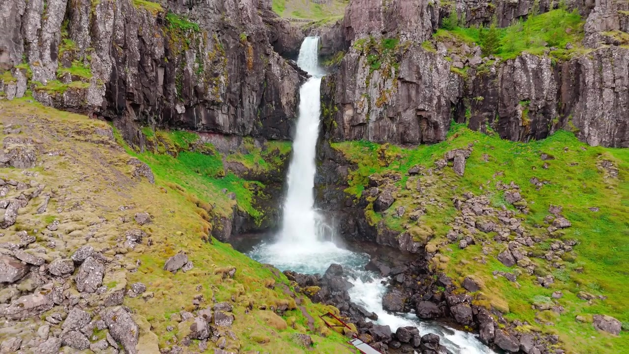Snaedalsfoss waterval die in een rotsachtige poel stort, omringd door bemoste kliffen, luchtbeeld met terugtrekkende beweging.