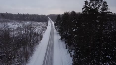 Luftaufnahme-Einer-Winterlichen-Straßengasse,-Umgeben-Von-Schneebedeckten-Bäumen-An-Bewölkten-Wintertagen,-Fallende-Kleine-Schneeflocken,-Durchfahrendes-Auto,-Vorwärts-Bewegende-Weitwinkel-Drohnenaufnahme