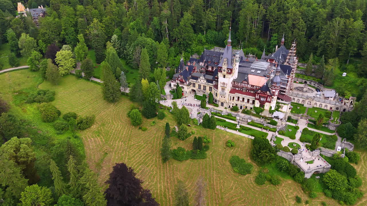Lots of tourists visiting the beautiful Peles Castle in Sinaia, the Carpathians, Romania. View on the building located in the pine tree wood from drone