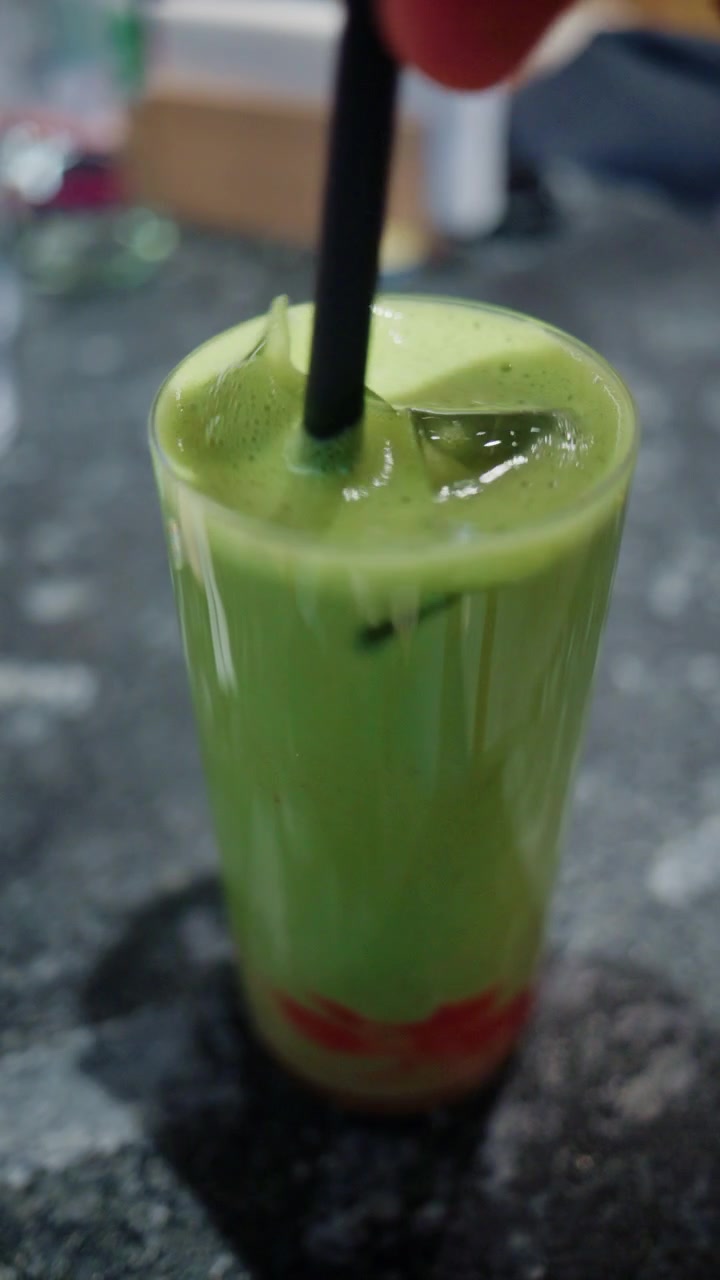 Primo piano di una bevanda verde colorata con una cannuccia nera su un tavolo da caffè.