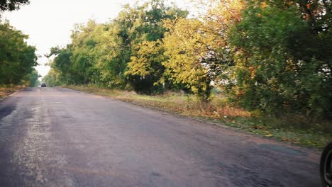 front view of a man in grey helmet and leather jacket and plaid shirt riding motorcycle on and asphalt road on sunny day in