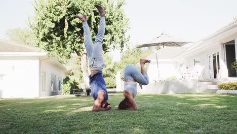 happy caucasian couple practicing yoga headstand pose in sunny garden, slow motion