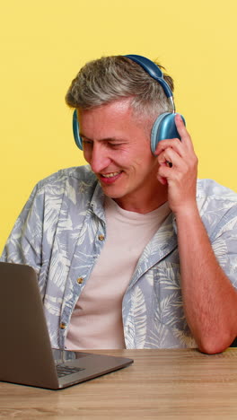 man in wireless headphones working on laptop at table nodding head enjoying favorite music sound