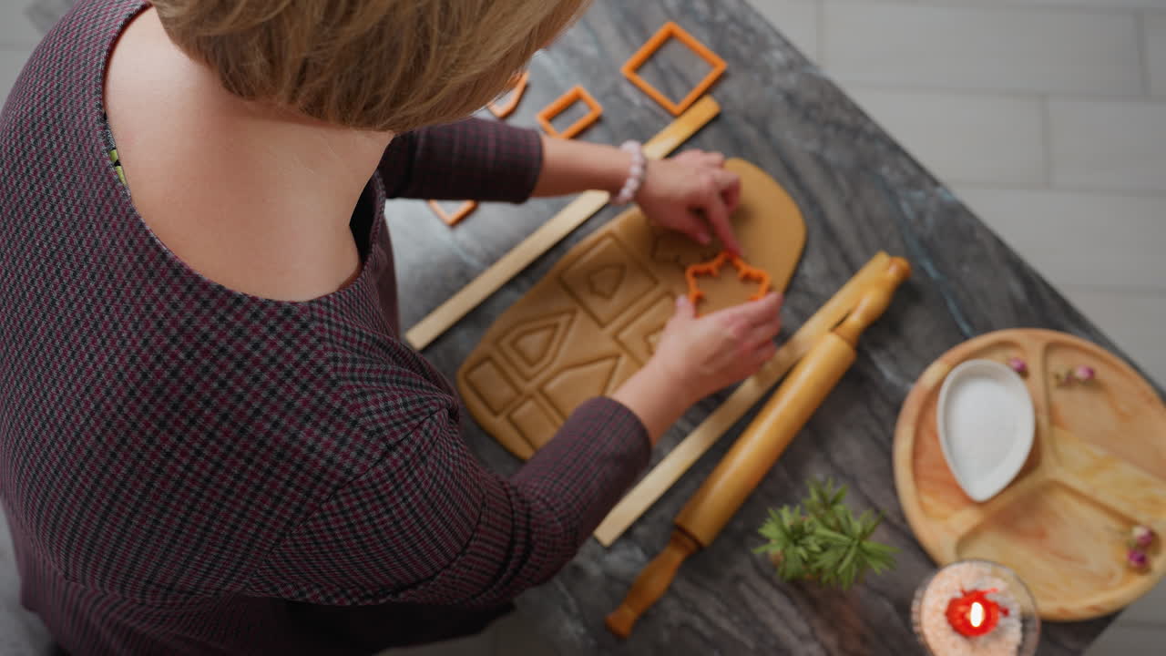 vista aérea de un panadero presionando un cortador de naranja sobre la masa enrollada, creando formas precisas, herramientas de horneado, rodillo y bandeja de madera con harina cerca