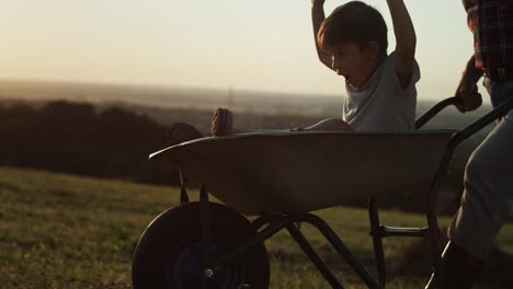 video of grandfather driving grandson in wheelbarrows at sunset