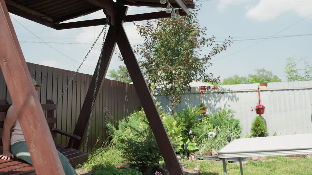 Girl Walking Past Backyard Playground With Younger Brother Following, Slide And Garden Visible, Sunlit Path And Casual Clothes, Playful Exploration And Curiosity, Suburban Home Setting