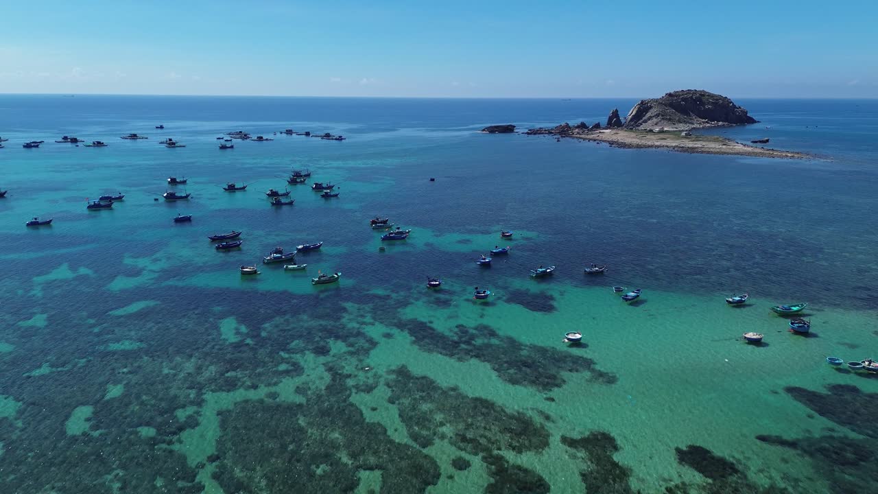 Aerial view of fishing village in Ninh Hải District, Ninh Thuận, featuring a smooth zoom in toward the anchored fishing boats surrounded by turquoise waters.