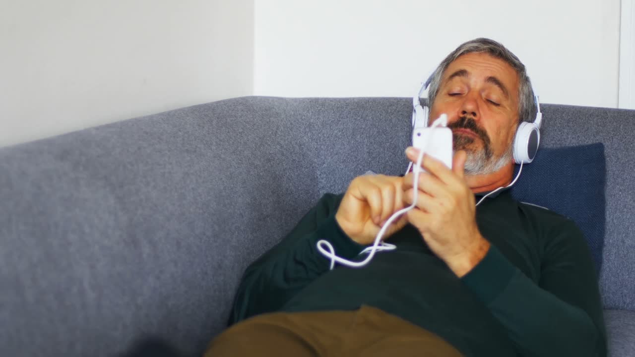 Man listening to music on mobile phone while lying on sofa 4k