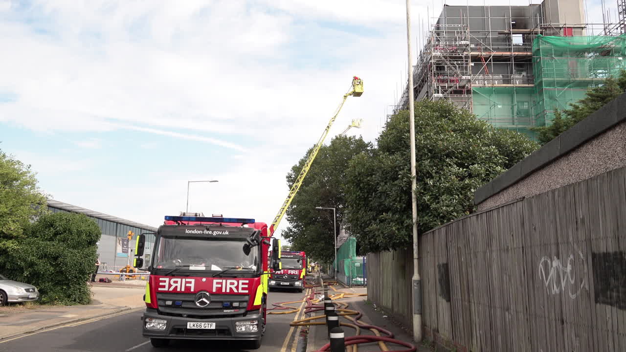 A firefighter ascends on a turntable ladder as second dowses down a tower block covered in flammable cladding that was destroyed by a fire.