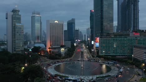 slow aerial dolly shot of busy traffic on a roundabout in modern city center in jakarta, indonesia