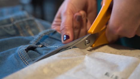 primer plano de manos cortando tela de denim con tijeras afiladas para el trabajo de costura