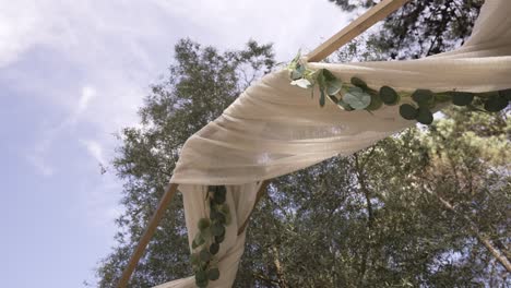 rustic wedding arch with draped fabric and eucalyptus greenery under a bright sky