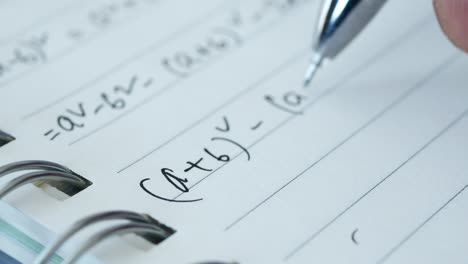 a closeup of a hand writing math equations in a notebook