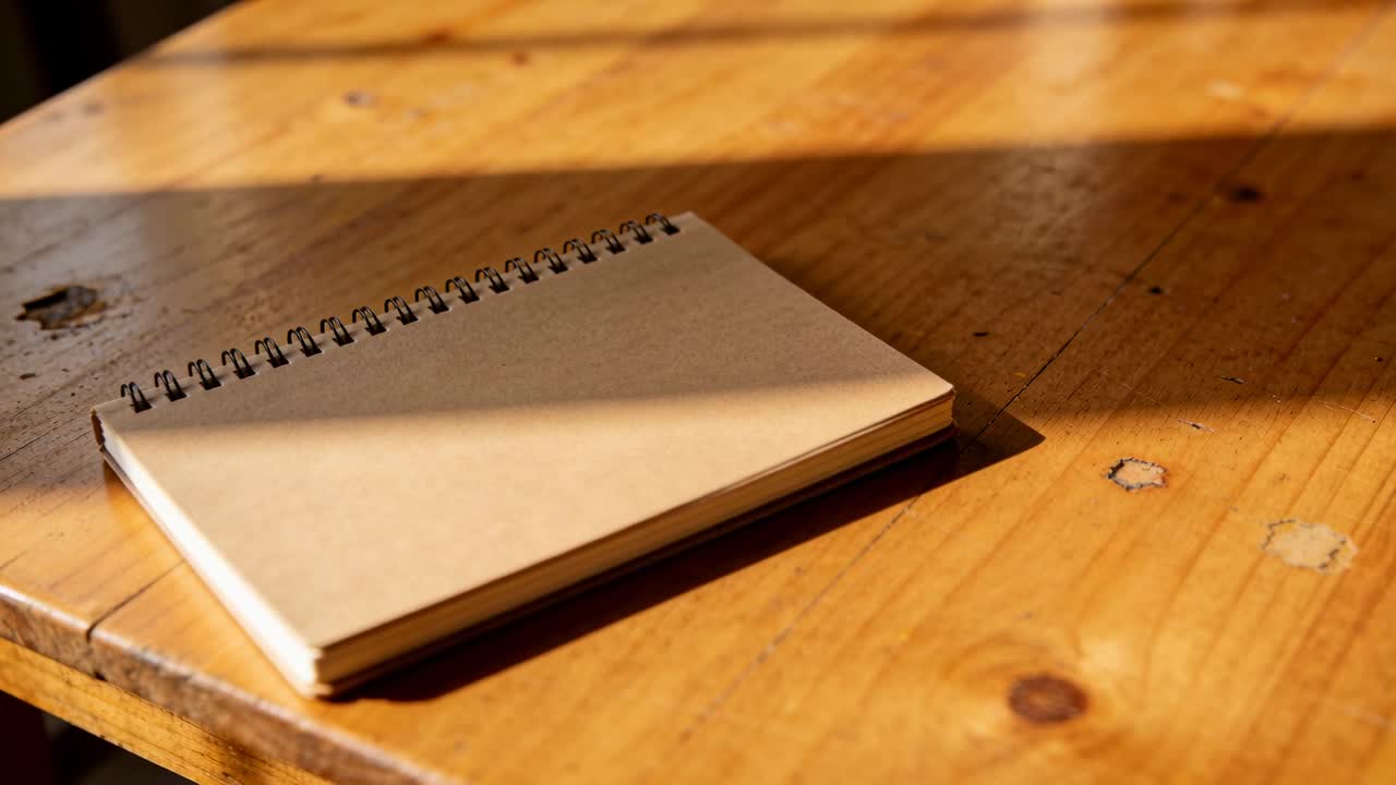 Bevægende kamera afslører en spiralbundet kraft-notesbog på et træbord, hvor et bånd af sollys i midten skifter.