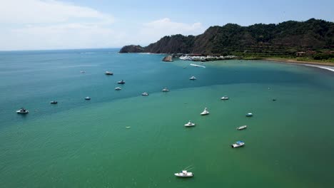 Boats-anchored-in-tropical-bay-with-waves-and-beach--aerial-rotating-view---Herradura-Beach,-Costa-Rica