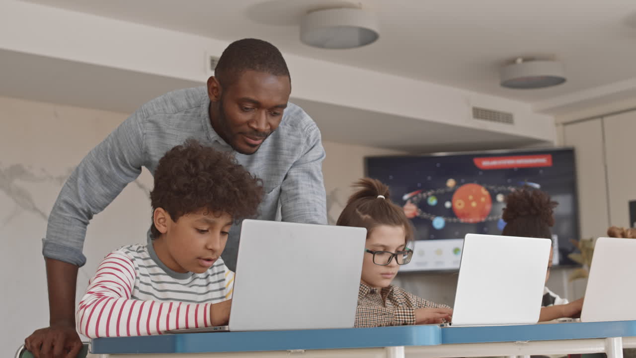 IT Teacher Helping Mixed-Race Student during Class