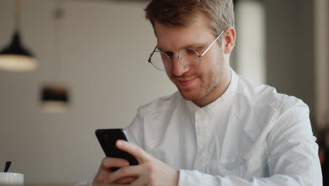 attractive man with glasses is viewing funny pictures and video in social media on smartphone display in cafe