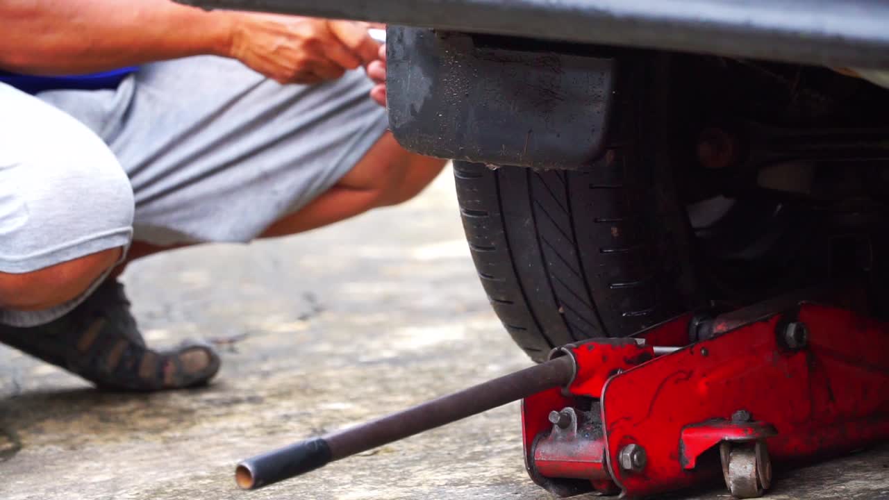 Close up shot of A man's hand is changing a car tire with a jack mounted under the car