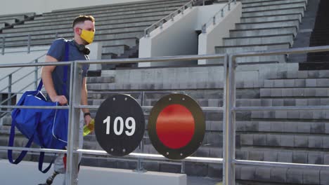 caucasian disabled male athlete with prosthetic leg wearing face mask, walking