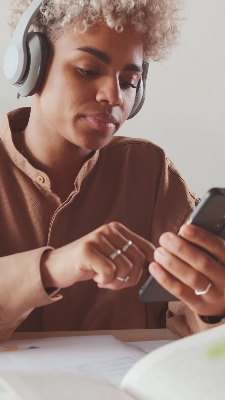 Giovane donna afroamericana che lavora con documenti e telefono, seduta alla scrivania.