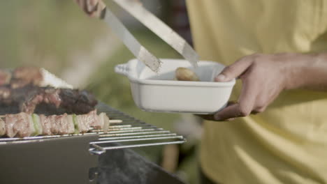 Close-up-of-man-putting-roasted-mushrooms-with-tongs-in-bowl