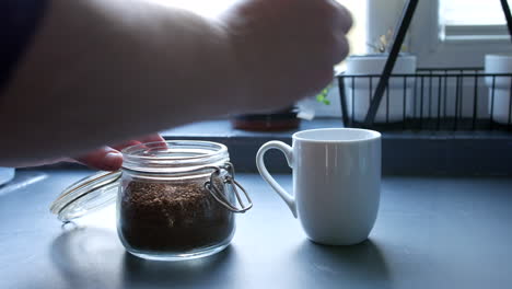 un hombre poniendo gránulos de café en una taza con una cuchara en la cocina