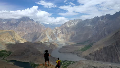 Drone-shot-of-passing-over-two-hikers-on-peak-at-Passu-Cones-Pakistan,-cinematic-wide-aerial-shot