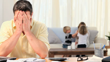 casual man calculating his bills with his family in the background