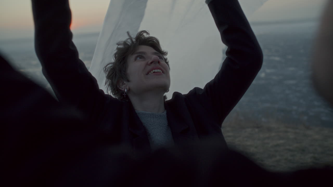Smiling Woman Holding Translucent Fabric Flowing in Breeze on Frozen Lake Shore
