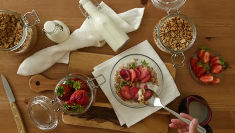 crop person eating healthy muesli with milk and strawberries