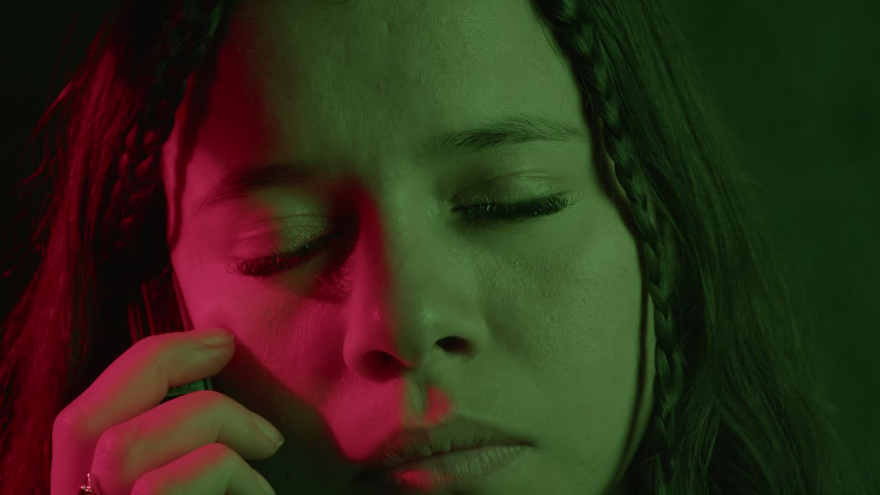 Intense close-up of woman holding phone, bathed in green and red light, conveying emotion and mystery. Sharp focus highlights details in a cinematic, moody atmosphere